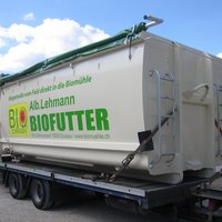 Abrollcontainer mit 38 m³ Volumen aus der Serie EKO2, grau lackiert mit Rollplane und Werbeaufdruck, stehend auf einem Anhänger