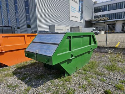 Grüne 7 m³-Absetzmulde mit beidseitig klappbarem Riffelblechdeckel, auf Kiesfläche vor Bürogebäude.